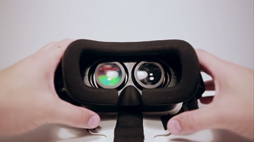 Hands Hold Black VR Headset on White Table
