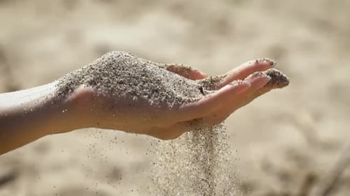La instantánea de la mano con arena esparcida a los dedos.