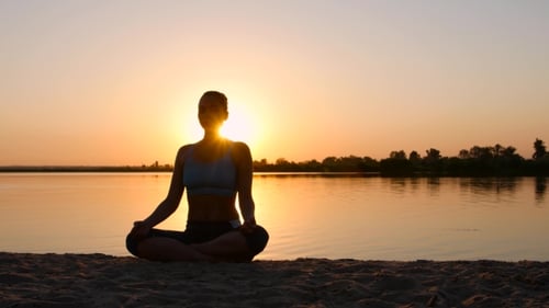 Woman Meditating on Beach at Sunrise
