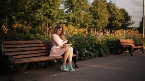 Beautiful Young Blond Woman Sitting On a Bench In The Summer Park And Reading a Book
