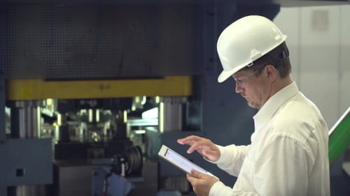 Engineer with Tablet Inspecting Machine in Factory