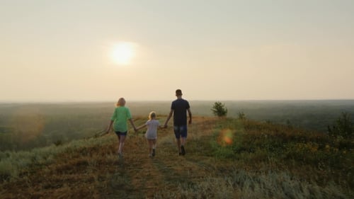 Family Walking on Hilltop at Sunset Holding Hands