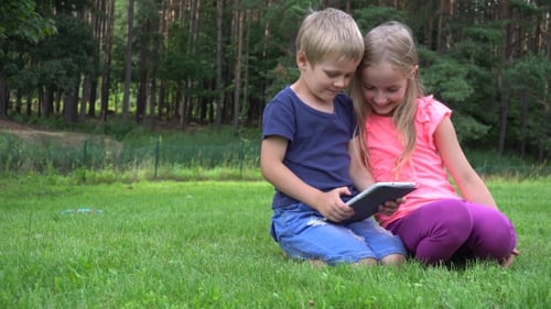 Children Using Tablet Device Together in Sunny Rural Setting