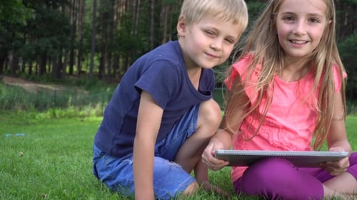 Children Sharing Tablet Outdoors in Grassy Woodland