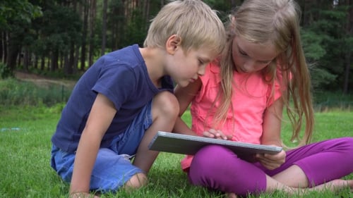 Boy and Girl Sharing Tablet Outdoors on Grass