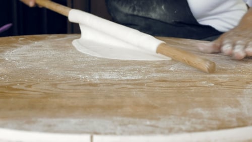 Hands Rolling Dough with Pin on Wooden Table