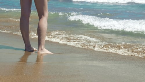 Female Stands On Wet Sand And Waves At The Beach