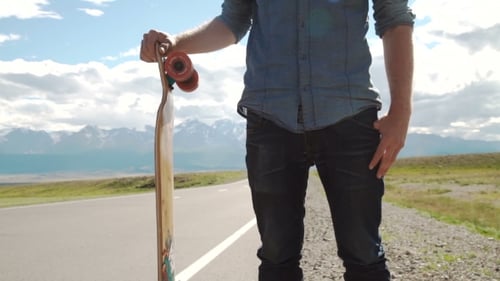 Man Stands with Longboard on Rural Road