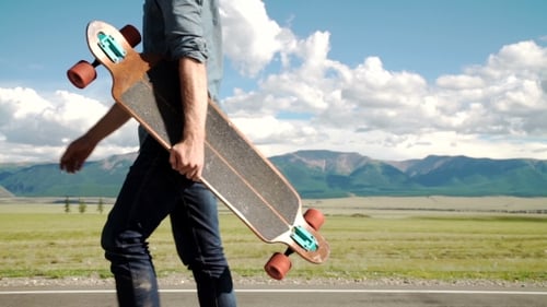 Young Adult Carrying Longboard on Scenic Road