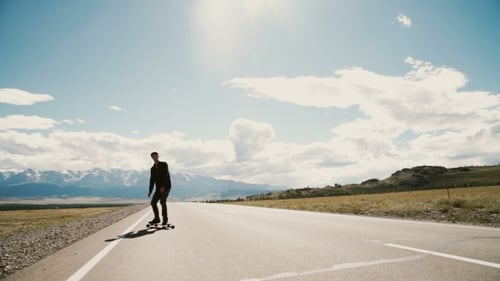 Man Longboarding on Open Road with Mountain View