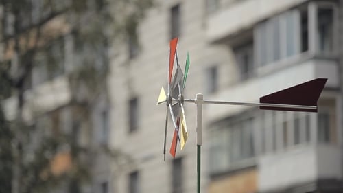 Eine helle Wetterfahne dreht sich mit einem Haus im Hintergrund.