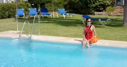 Lifeguard In Red Swimsuit Sitting At Edge Of Pool