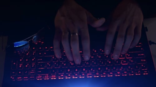 Hands Typing on Red Backlit Computer Keyboard