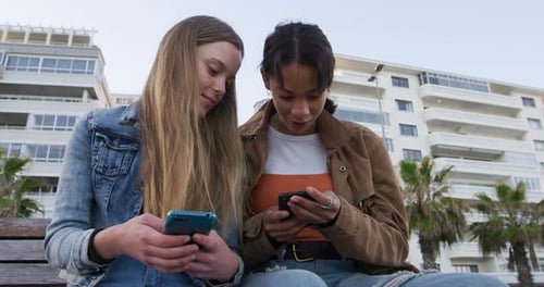 Front view of a Caucasian and a mixed race girl using their phones