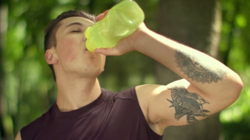 Tired Sport Man Drinks Water From Plastic Bottle After Marathon In Park