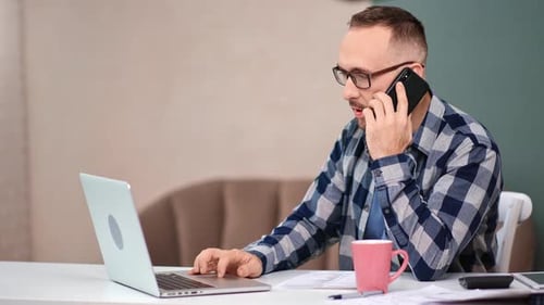 Adult Working at Laptop While on Cell Phone