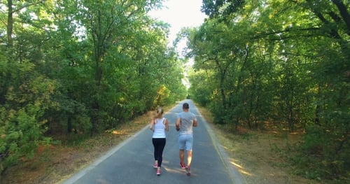 Aerial View Of Couple Jogging Along Road In Forest