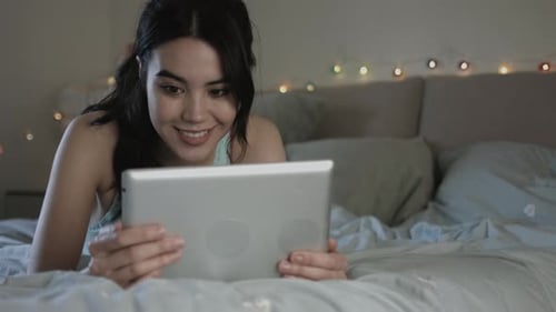 Woman Relaxes in Bed Using Tablet at Night