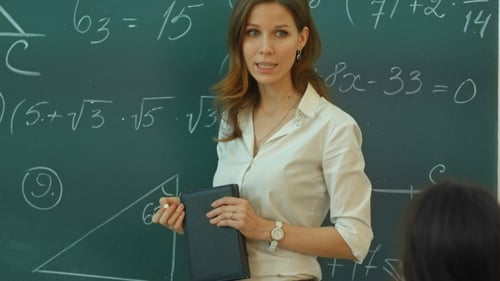 Female Teacher Writing Equations on Chalkboard in Classroom