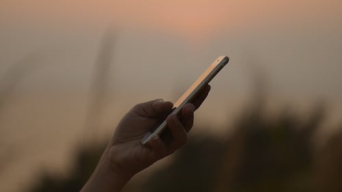 Hand Holds Smart Phone at Sunset Outdoors