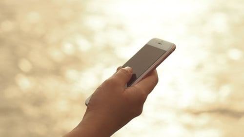 Hand Holding Smartphone at Golden Hour on Beach