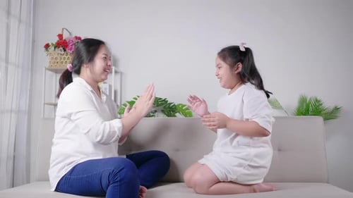 mom and kid sitting and playing hands game together with happy and laughing face on sofa
