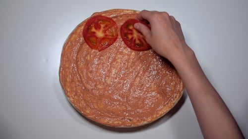 Frauenhände legen Tomatenscheibe auf rundem Teig aus, um Pizza zuzubereiten
