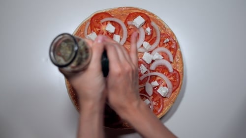 Frauenhände streuen Gewürze aus der Mühle auf griechische Pizza mit Feta-Käse