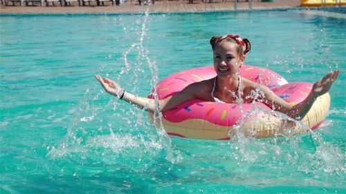 Tiro de ângulo baixo da água azul da piscina e da menina espirrando enquanto segura. 20S. 1080p.