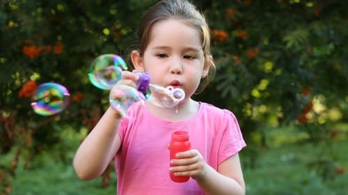 Happy Child Blowing Soap Bubbles In Park