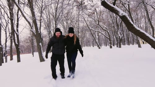 Ein junges Paar zieht in den Winterwald und geht auf einem schmalen Pfad durch Tiefschnee