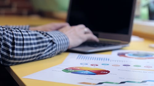 Hands Typing on Laptop with Business Graphs