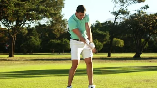 Male Golfer Swings Club on Golf Course Green
