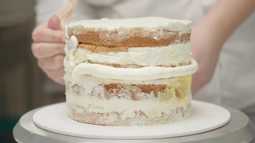 Baker Decorating Tiered Cake with White Frosting