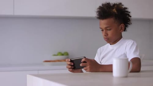 Boy Plays Game on Phone in Kitchen