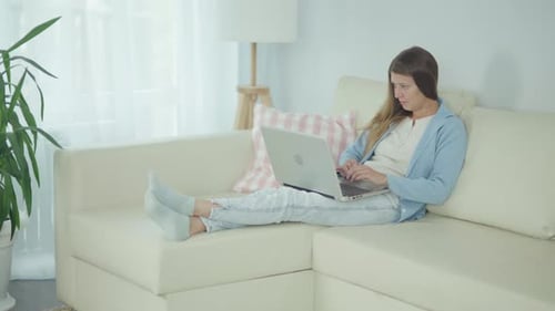 Woman Using Laptop on Couch in Living Room