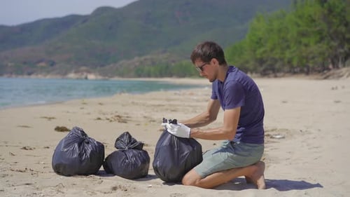 Man in Gloves Collects Plastic Trash on a Beach. The Problem of Garbage on the Beach Sand Caused By