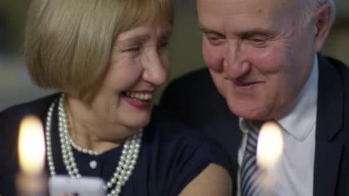 Senior Couple Smiles Using Smartphone at Candlelight Dinner