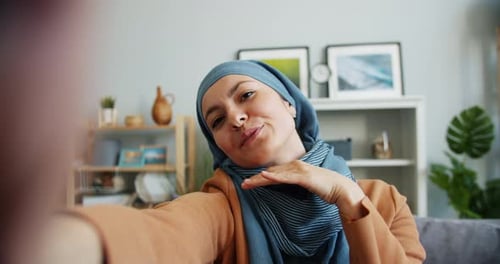 POV einer Frau aus dem Nahen Osten im Hijab beim Selfie zu Hause mit Blick in die Kamera
