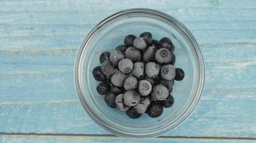 Frozen Blueberries in Glass Bowl on Blue Surface