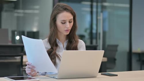 Businesswoman with Headache Reviewing Paperwork at Desk