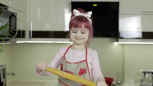 Little Child Girl in the Kitchen Dressed in Apron and Scarf with Rolling Pin