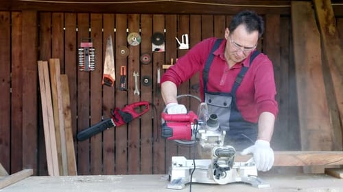 Männlicher Tischler bearbeitet Holzbalken mit einer Gehrungssäge in einer Werkstatt.