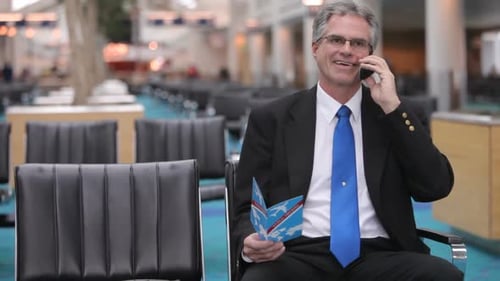 Mature business sits in airport lobby talking on cell phone