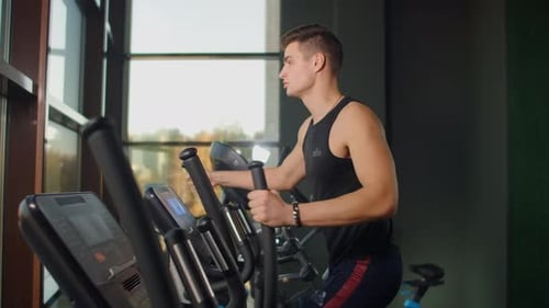 Back View a Man in the Cardio Area of the Gym Trains on an Elliptical Trainer