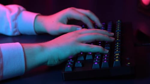 A Young Man Is Typing on a Computer Keyboard. Hands Close Up. Blue and Red Light Falls on the Hands.