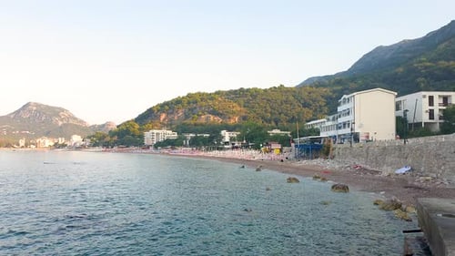 Slow motion footage of beach on the sea with hotels and mountain in the background.