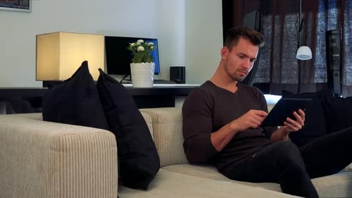 Young Man Relaxing With Tablet on Couch Indoors