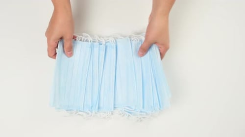 Hands Spreading Light Blue Surgical Masks on White Surface