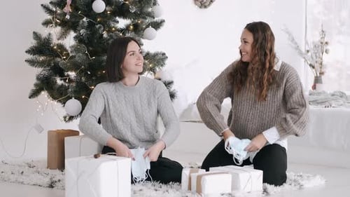 Dos mujeres atractivas sentadas bajo el árbol de Navidad y lanzando máscaras al aire